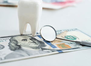 A tooth and a dental instrument over a dollar bill
